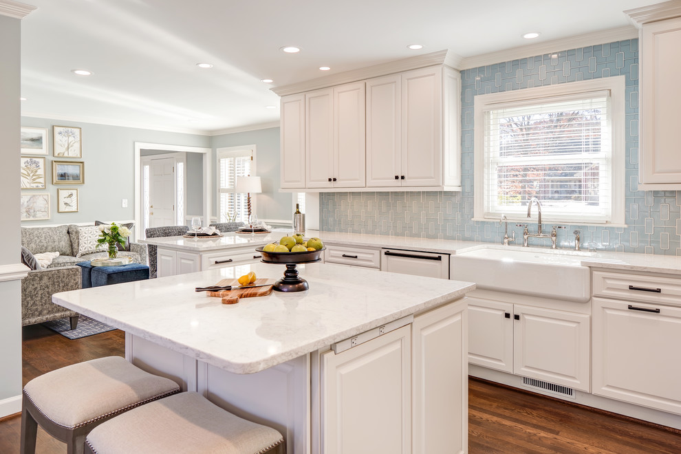 Example of a mid-sized transitional u-shaped medium tone wood floor and brown floor eat-in kitchen design with a farmhouse sink, raised-panel cabinets, white cabinets, quartz countertops, blue backsplash, porcelain backsplash, paneled appliances and an island