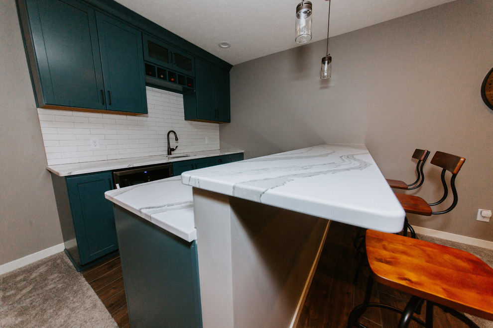 Photo of a small transitional galley seated home bar in Omaha with an undermount sink, shaker cabinets, green cabinets, marble benchtops, white splashback, subway tile splashback, medium hardwood floors, brown floor and white benchtop.