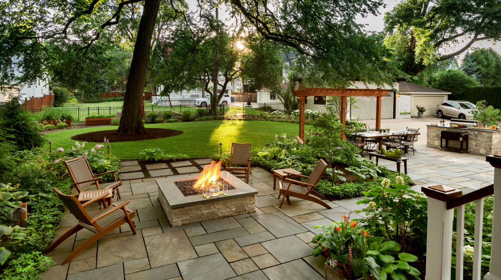 Photo of a large traditional backyard patio with a fire feature and natural stone pavers.