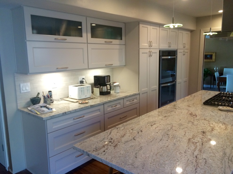 Photo of a mid-sized traditional single-wall kitchen pantry in Salt Lake City with an undermount sink, recessed-panel cabinets, white cabinets, granite benchtops, white splashback, porcelain splashback, stainless steel appliances, bamboo floors and with island.