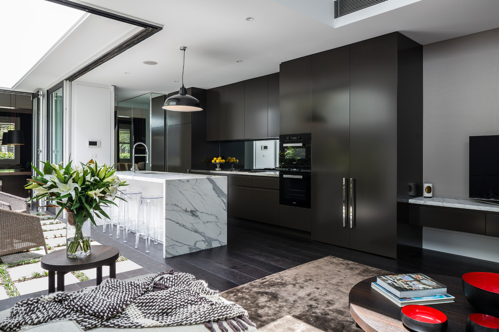 This is an example of a mid-sized contemporary galley open plan kitchen in Sydney with an undermount sink, marble benchtops, mirror splashback, black appliances, dark hardwood floors, with island, brown floor, white benchtop, flat-panel cabinets and black cabinets.