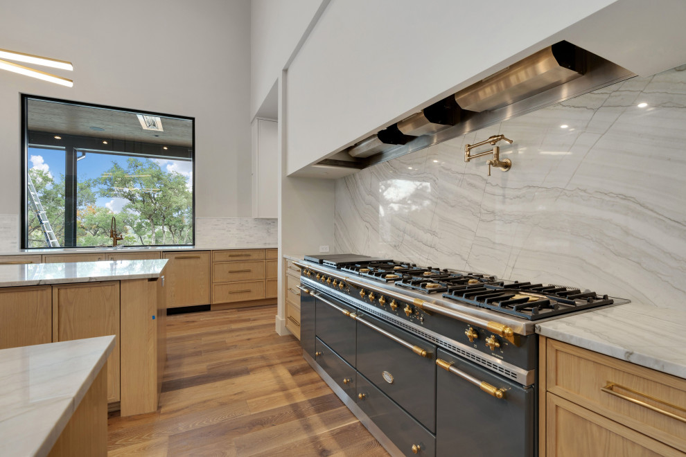 Large kitchen photo with light wood cabinets, white backsplash, stone slab backsplash, stainless steel appliances, two islands and white countertops