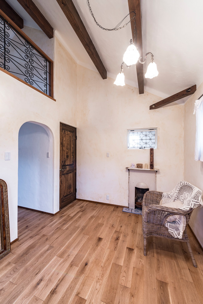 Immagine di una piccola camera matrimoniale mediterranea con pareti bianche, parquet chiaro, stufa a legna, cornice del camino in mattoni e pavimento marrone