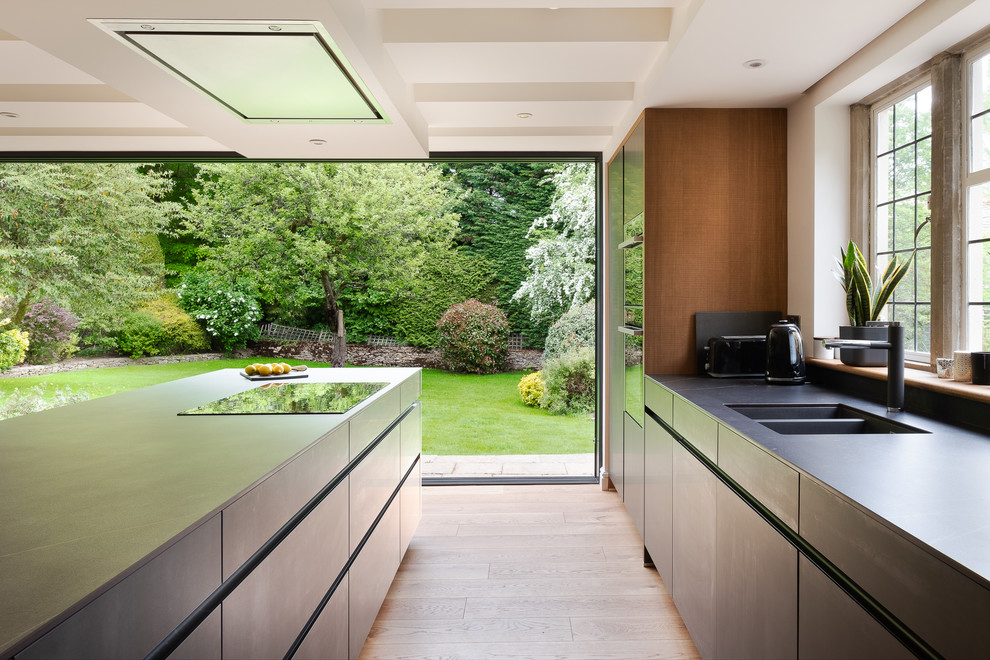 Design ideas for a large contemporary galley kitchen in Gloucestershire with a double-bowl sink, flat-panel cabinets, grey cabinets, solid surface benchtops, grey splashback, black appliances, porcelain floors, with island, beige floor and grey benchtop.