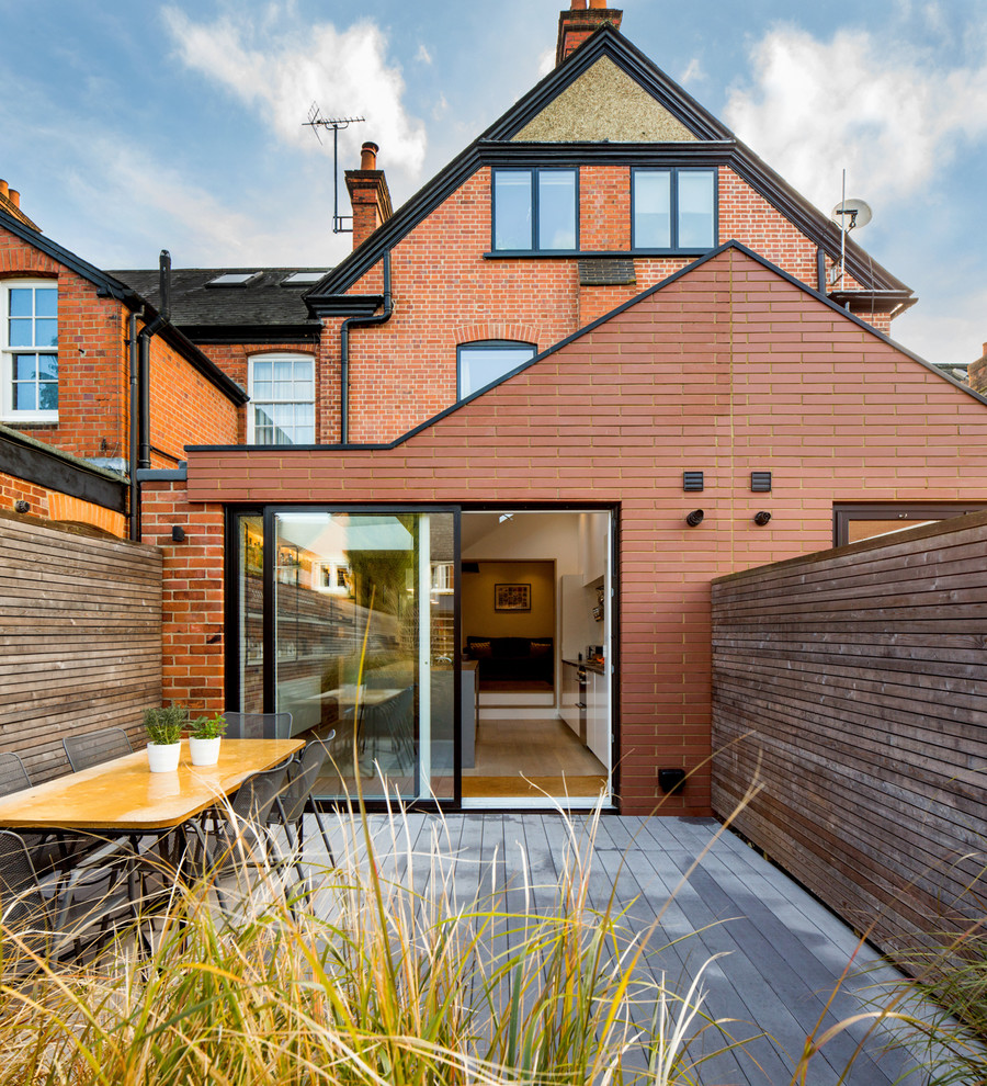 This is an example of a mid-sized transitional three-storey brick red townhouse exterior in London with a gable roof.