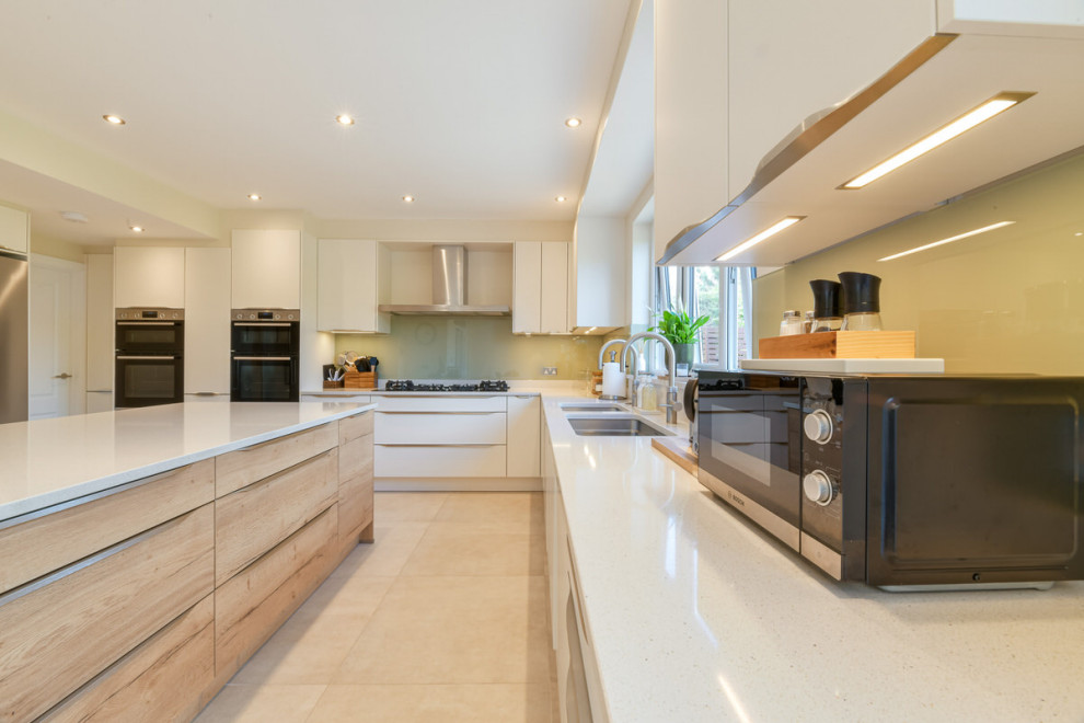 This is an example of a large modern l-shaped open plan kitchen in London with a double-bowl sink, shaker cabinets, white cabinets, limestone benchtops, grey splashback, slate splashback, stainless steel appliances, with island and white benchtop.
