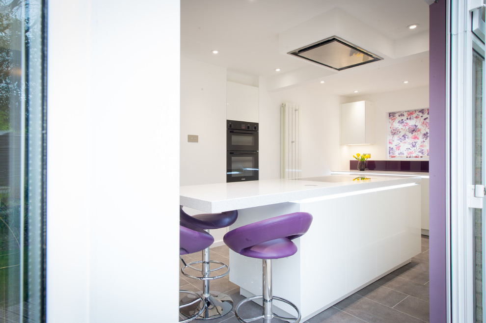Photo of a mid-sized contemporary open plan kitchen in Other with white cabinets, pink splashback, black appliances, ceramic floors, with island, grey floor, a drop-in sink, flat-panel cabinets, quartzite benchtops and glass sheet splashback.