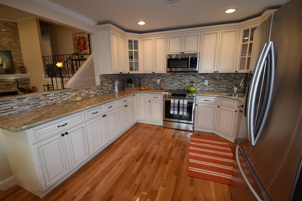 Example of a mid-sized transitional u-shaped medium tone wood floor eat-in kitchen design in New York with an undermount sink, raised-panel cabinets, white cabinets, granite countertops, gray backsplash, glass tile backsplash, stainless steel appliances and a peninsula