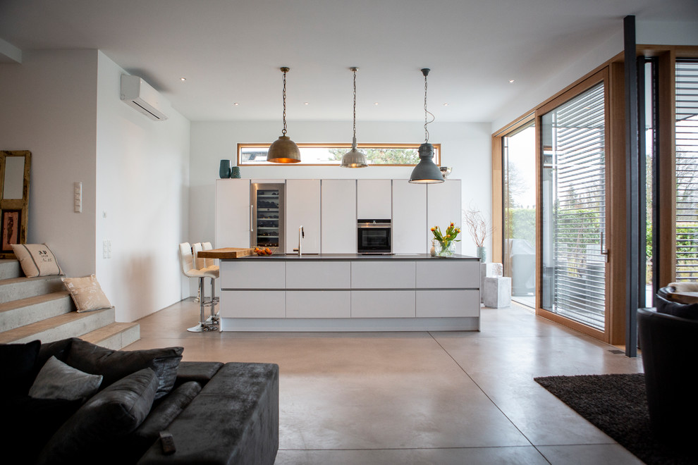 Photo of an industrial galley open plan kitchen in Frankfurt with an undermount sink, flat-panel cabinets, white cabinets, granite benchtops, white splashback, window splashback, stainless steel appliances, cement tiles, with island, grey floor and black benchtop.