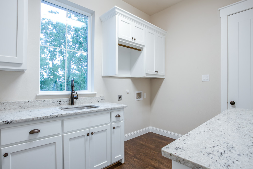 Design ideas for a large country galley utility room in Dallas with an undermount sink, shaker cabinets, white cabinets, granite benchtops, grey walls, medium hardwood floors, a stacked washer and dryer and brown floor.