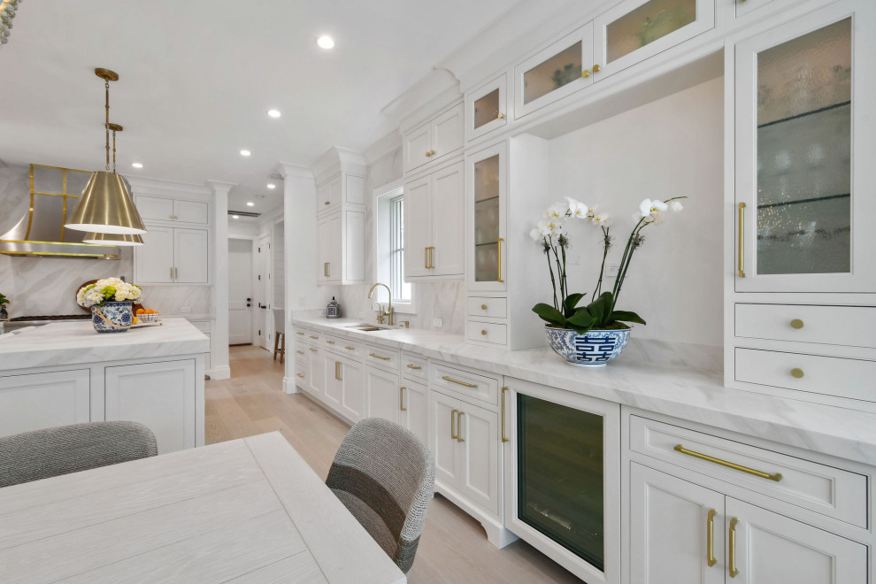 Klassisk inredning av ett stort vit vitt kök och matrum, med en undermonterad diskho, luckor med profilerade fronter, vita skåp, bänkskiva i kvartsit, vitt stänkskydd, stänkskydd i sten, integrerade vitvaror, ljust trägolv, en köksö och brunt golv
