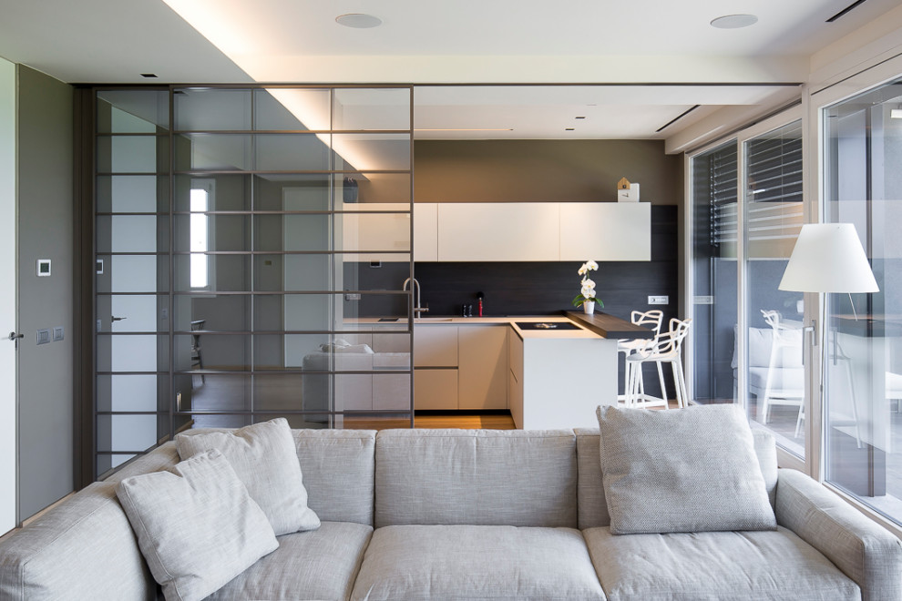 This is an example of an expansive modern l-shaped open plan kitchen in Other with an integrated sink, glass-front cabinets, white cabinets, solid surface benchtops, grey splashback, timber splashback, panelled appliances, medium hardwood floors, a peninsula, brown floor, white benchtop and recessed.