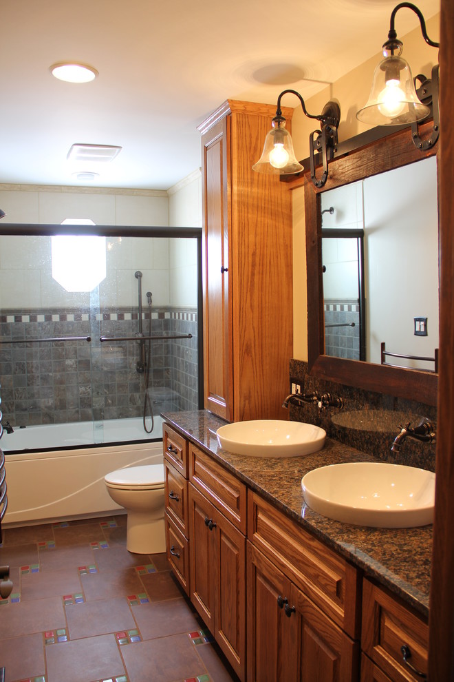 Tub/shower combo - transitional brown tile and porcelain tile porcelain tile tub/shower combo idea in Columbus with a vessel sink, an undermount tub, a two-piece toilet, raised-panel cabinets, medium tone wood cabinets, granite countertops and beige walls
