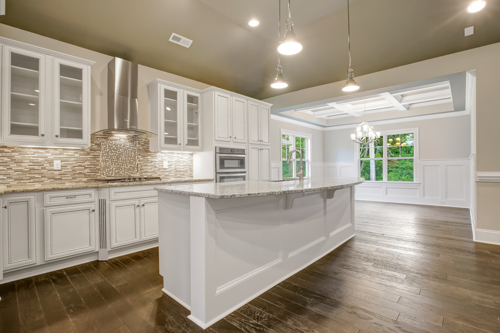 Open concept kitchen - mid-sized transitional l-shaped dark wood floor open concept kitchen idea with a farmhouse sink, recessed-panel cabinets, white cabinets, granite countertops, beige backsplash, mosaic tile backsplash, stainless steel appliances and an island
