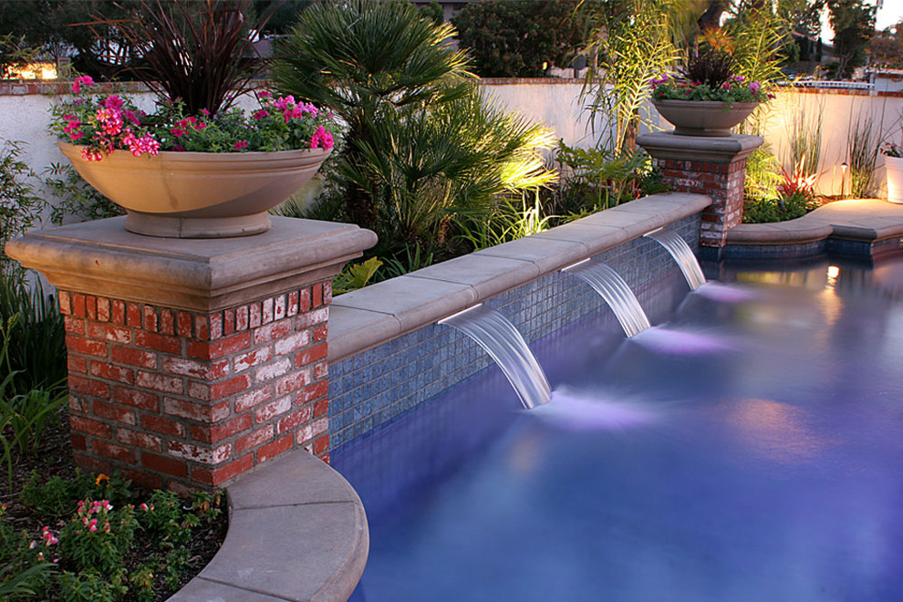 This is an example of a mid-sized traditional backyard lap pool in Orange County with a water feature and natural stone pavers.