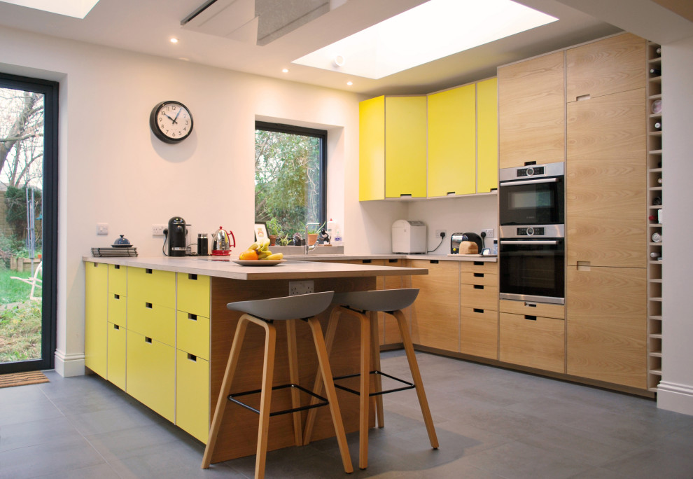Photo of a mid-sized midcentury u-shaped open plan kitchen in Other with a drop-in sink, flat-panel cabinets, yellow cabinets, concrete benchtops, stainless steel appliances, ceramic floors, a peninsula, grey floor and grey benchtop.