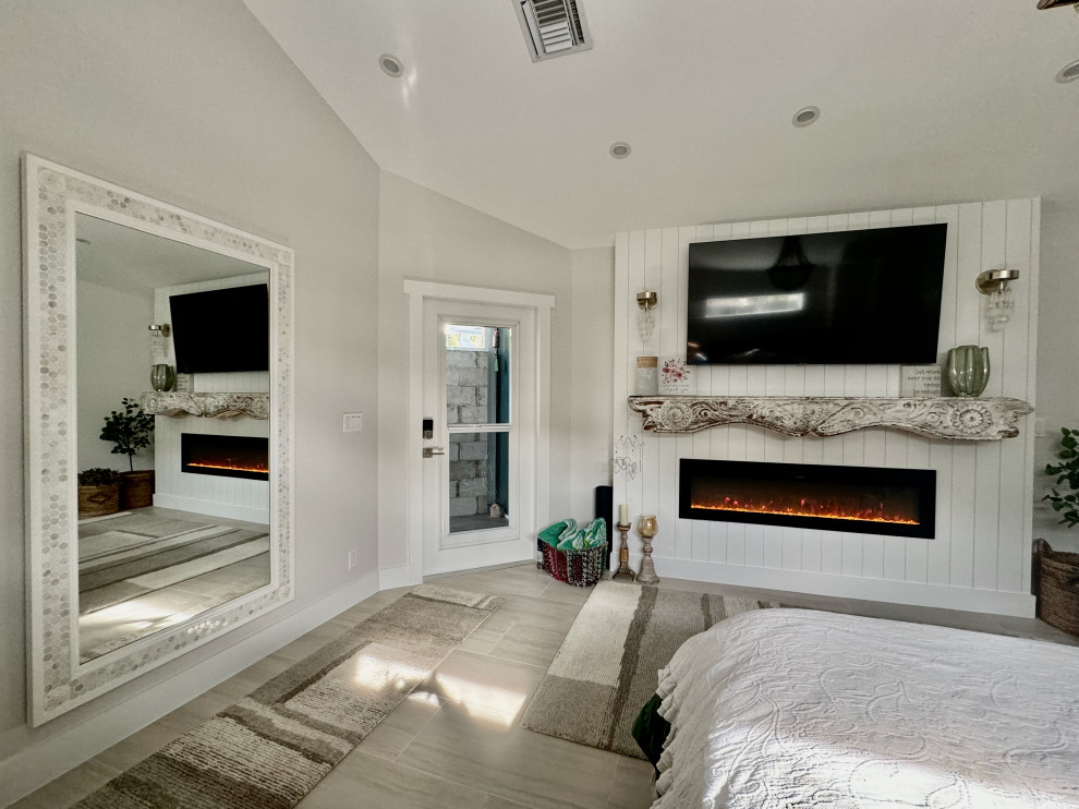 Großes Stilmix Hauptschlafzimmer mit beiger Wandfarbe, Porzellan-Bodenfliesen, Hängekamin, Kaminumrandung aus Holz, beigem Boden und gewölbter Decke in Miami