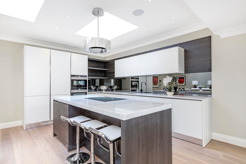 This is an example of a contemporary l-shaped eat-in kitchen in London with an undermount sink, flat-panel cabinets, white cabinets, mirror splashback, light hardwood floors and with island.