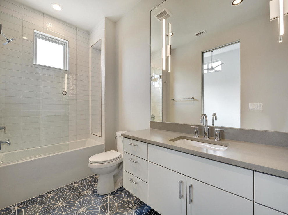 Photo of a large contemporary master bathroom in Austin with flat-panel cabinets, white cabinets, an alcove tub, a shower/bathtub combo, a two-piece toilet, white tile, subway tile, white walls, mosaic tile floors, an undermount sink, engineered quartz benchtops, grey floor and a shower curtain.