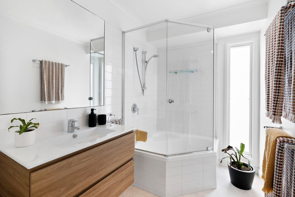 Inredning av ett modernt litet vit vitt badrum med dusch, med släta luckor, skåp i ljust trä, ett platsbyggt badkar, en hörndusch, vit kakel, terrazzogolv, ett integrerad handfat, bänkskiva i akrylsten och dusch med gångjärnsdörr