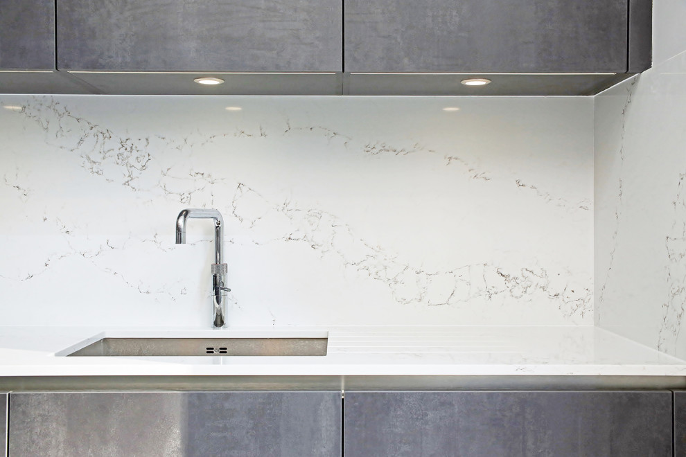Inspiration for a mid-sized contemporary single-wall open plan kitchen in Surrey with an undermount sink, flat-panel cabinets, black cabinets, quartzite benchtops, white splashback, stone slab splashback, black appliances, concrete floors, with island and white floor.