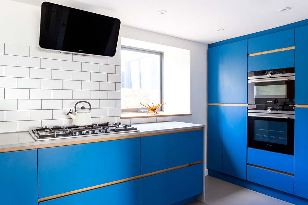 This is an example of a mid-sized contemporary u-shaped eat-in kitchen in Wiltshire with an undermount sink, flat-panel cabinets, blue cabinets, white splashback, stone tile splashback, stainless steel appliances, concrete floors and no island.