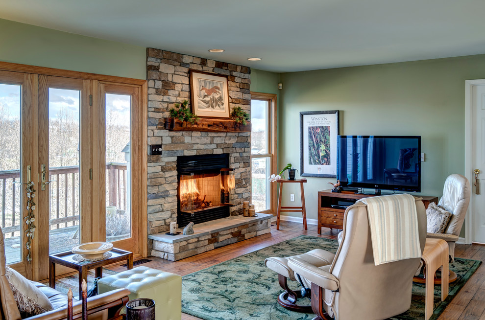 Photo of a transitional family room in Other with green walls, medium hardwood floors, a standard fireplace, a stone fireplace surround and brown floor.