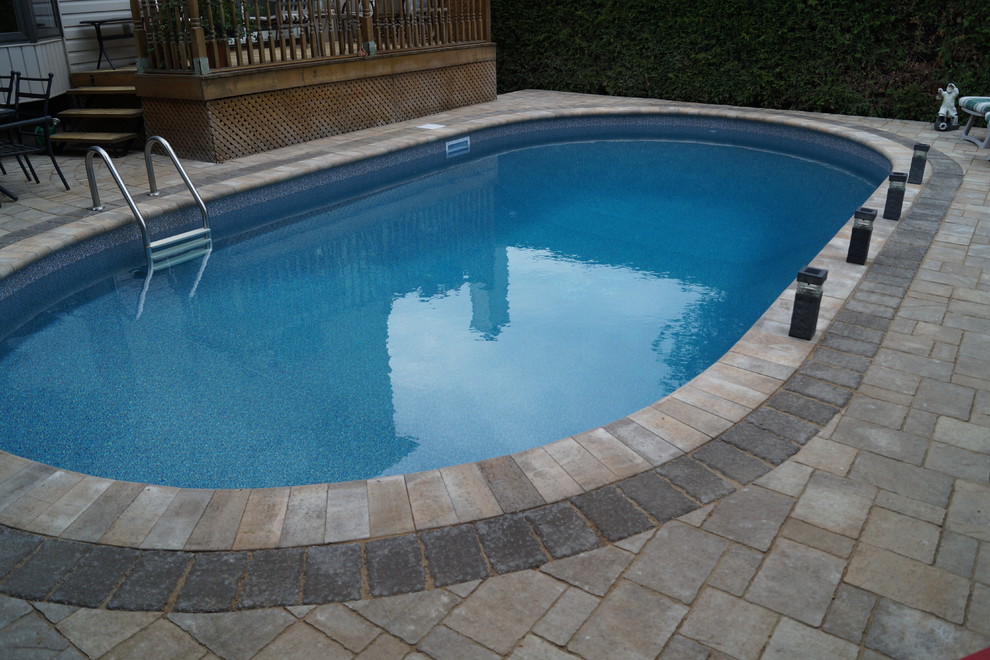 Photo of a mid-sized traditional backyard pool in Ottawa with a water feature and concrete pavers.