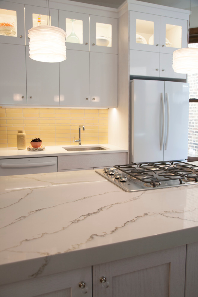 Inspiration for a mid-sized transitional l-shaped eat-in kitchen in Chicago with an undermount sink, flat-panel cabinets, white cabinets, quartz benchtops, yellow splashback, ceramic splashback, white appliances, medium hardwood floors and with island.