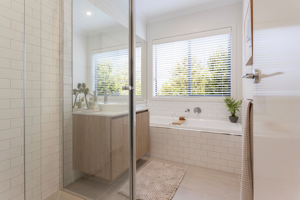 This is an example of a beach style bathroom in Melbourne with flat-panel cabinets, light wood cabinets, a drop-in tub, white tile, subway tile, white walls, a vessel sink, beige floor and white benchtops.