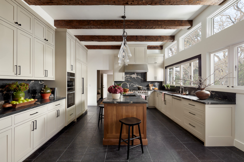 Inspiration for a transitional u-shaped kitchen in San Francisco with an undermount sink, recessed-panel cabinets, white cabinets, black splashback, stone slab splashback, stainless steel appliances, with island, black floor, black benchtop and exposed beam.