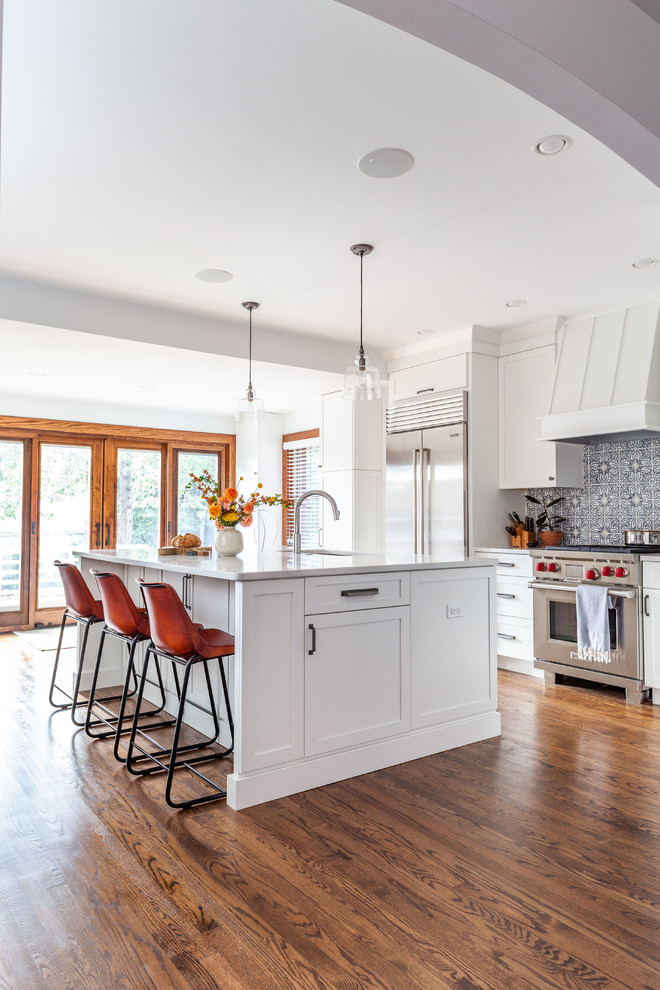 Transitional dark wood floor and brown floor kitchen photo in Chicago with shaker cabinets, white cabinets, quartz countertops, multicolored backsplash, stone tile backsplash, stainless steel appliances, an island and white countertops