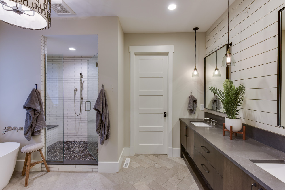 Mid-sized country master bathroom in Minneapolis with furniture-like cabinets, brown cabinets, a freestanding tub, an alcove shower, a one-piece toilet, white tile, subway tile, grey walls, limestone floors, a drop-in sink, engineered quartz benchtops, grey floor, a hinged shower door and grey benchtops.