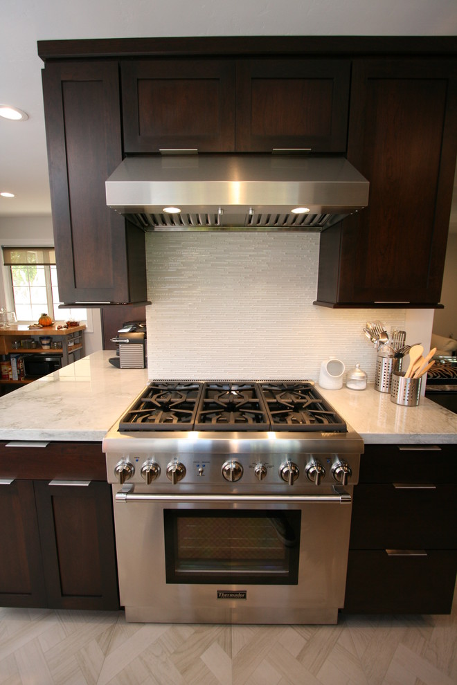 Inspiration for a mid-sized transitional l-shaped porcelain tile kitchen remodel in Orange County with a double-bowl sink, recessed-panel cabinets, dark wood cabinets, quartzite countertops, white backsplash, glass tile backsplash, stainless steel appliances and no island