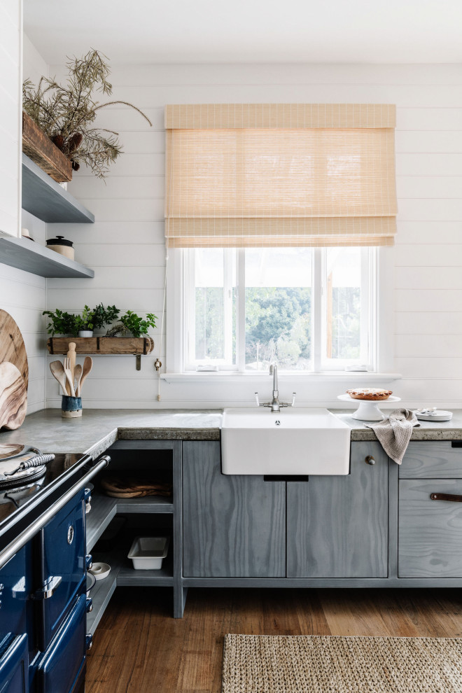 This is an example of a mid-sized beach style u-shaped eat-in kitchen in Melbourne with a farmhouse sink, open cabinets, concrete benchtops, white splashback, shiplap splashback, coloured appliances, light hardwood floors and grey benchtop.