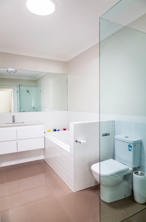 Design ideas for a contemporary kids bathroom in Melbourne with an undermount sink, white cabinets, a corner tub, a corner shower, a two-piece toilet, white tile, ceramic floors and white walls.