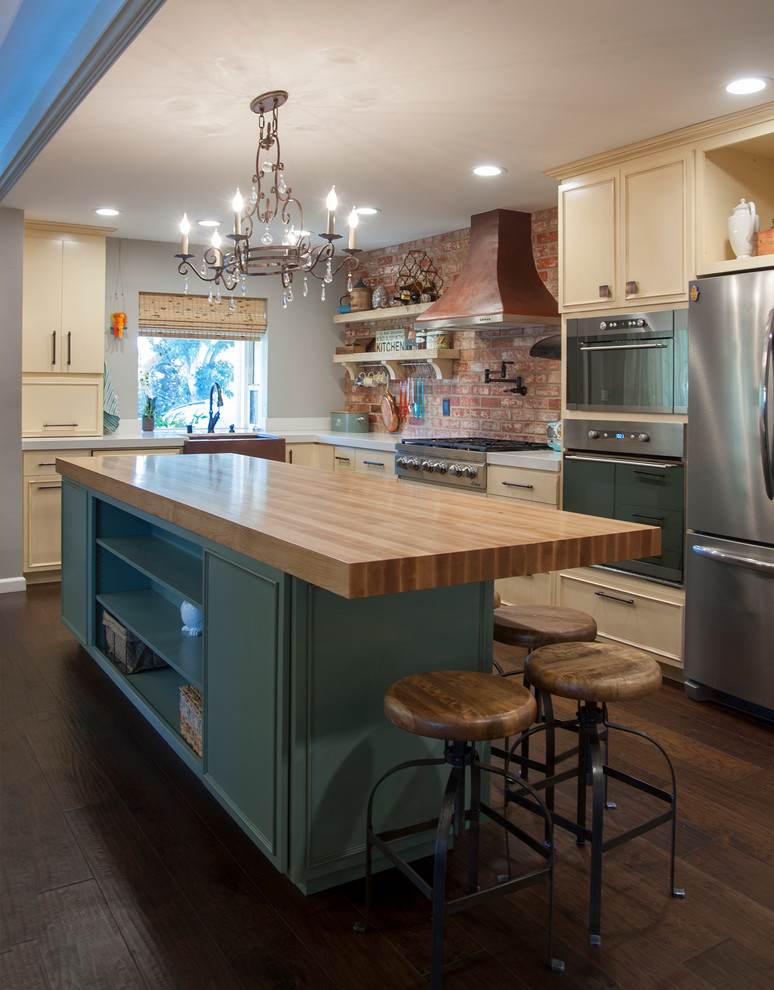 Photo of a mid-sized traditional l-shaped open plan kitchen in San Francisco with a farmhouse sink, raised-panel cabinets, blue cabinets, quartz benchtops, orange splashback, terra-cotta splashback, stainless steel appliances, medium hardwood floors and with island.