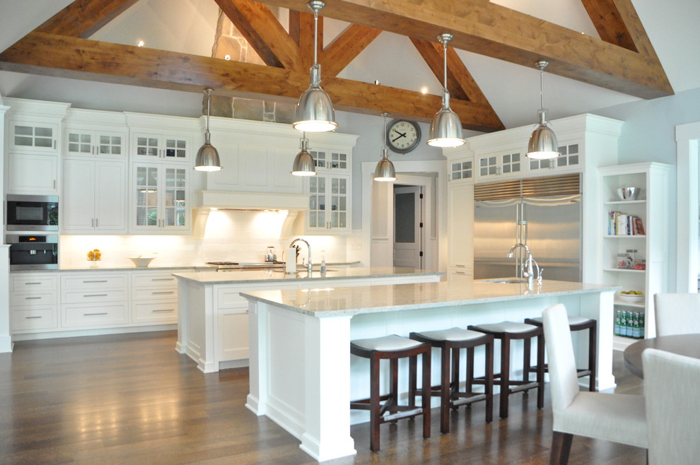 This is an example of a large transitional l-shaped eat-in kitchen in Cleveland with an undermount sink, recessed-panel cabinets, white cabinets, marble benchtops, white splashback, subway tile splashback, stainless steel appliances, medium hardwood floors, multiple islands, brown floor and white benchtop.