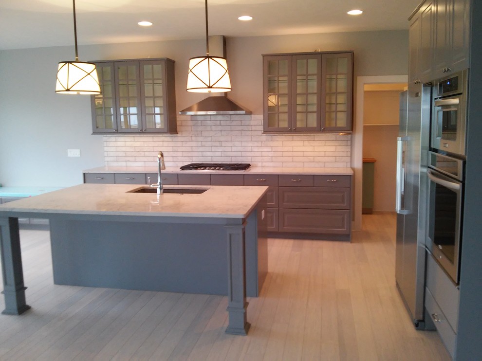 This is an example of a large modern eat-in kitchen in Omaha with an undermount sink, grey cabinets, white splashback, ceramic splashback, stainless steel appliances, bamboo floors and with island.