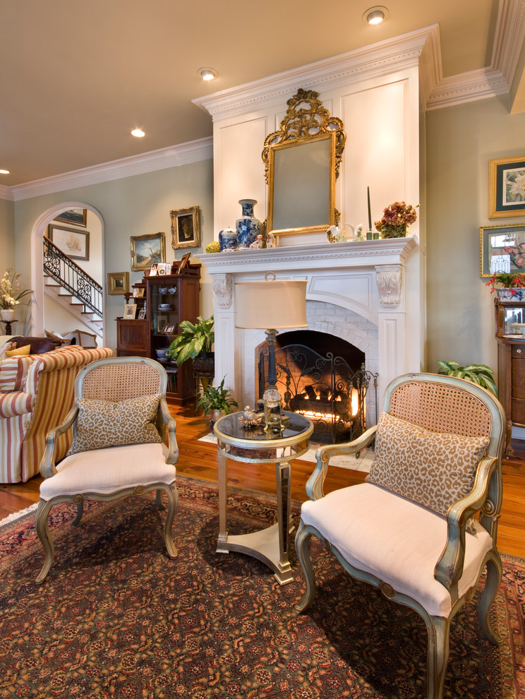 This is an example of a large traditional living room in New Orleans with green walls, light hardwood floors, a standard fireplace and a wood fireplace surround.