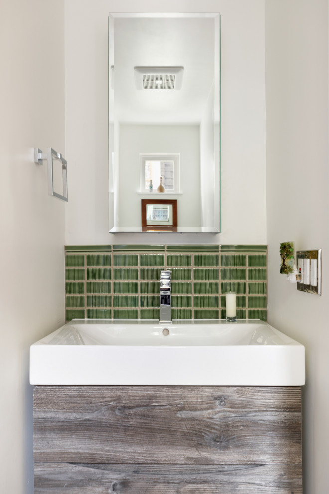 Small transitional powder room in Seattle with flat-panel cabinets, distressed cabinets, a wall-mount toilet, green tile, ceramic tile, multi-coloured walls, porcelain floors, a wall-mount sink, brown floor and a floating vanity.