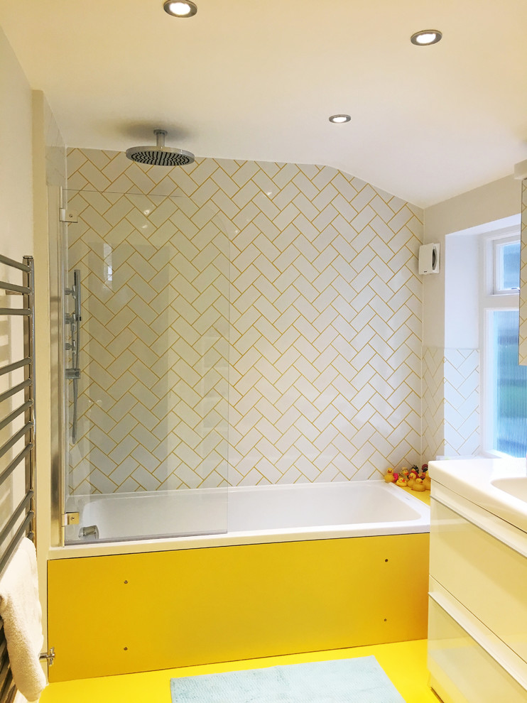 Mid-sized contemporary kids bathroom in London with flat-panel cabinets, white cabinets, a drop-in tub, a shower/bathtub combo, subway tile, white walls, vinyl floors, a drop-in sink, yellow floor and a hinged shower door.