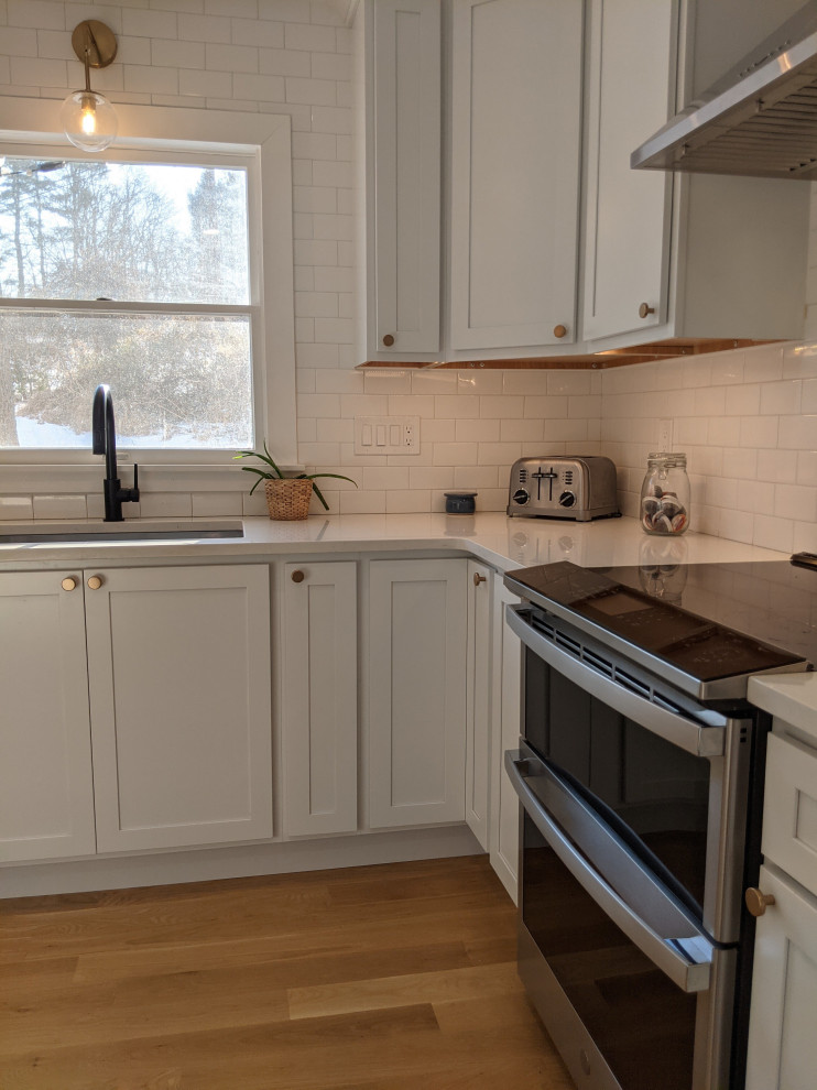 Klassisk inredning av ett mellanstort vit vitt kök, med en undermonterad diskho, skåp i shakerstil, vita skåp, bänkskiva i kvartsit, vitt stänkskydd, stänkskydd i tunnelbanekakel, rostfria vitvaror, ljust trägolv, en köksö och brunt golv