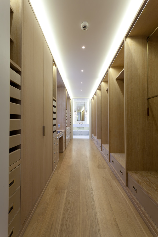 Large modern walk-in wardrobe in London with light wood cabinets and light hardwood floors.