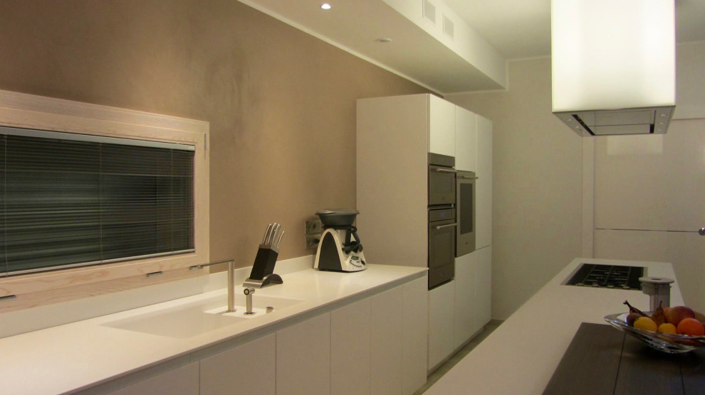 This is an example of a large modern galley open plan kitchen in Bologna with an integrated sink, flat-panel cabinets, white cabinets, solid surface benchtops, stainless steel appliances, concrete floors, with island, beige floor and white benchtop.