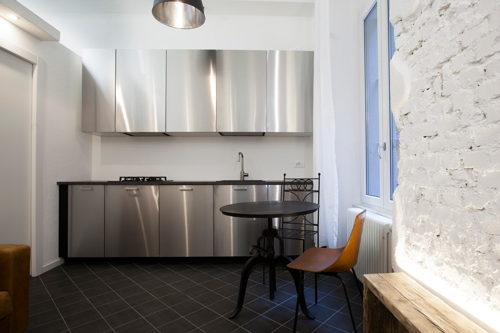 Photo of a small industrial single-wall open plan kitchen in Milan with a drop-in sink, stainless steel cabinets, stainless steel appliances, porcelain floors, no island and black floor.