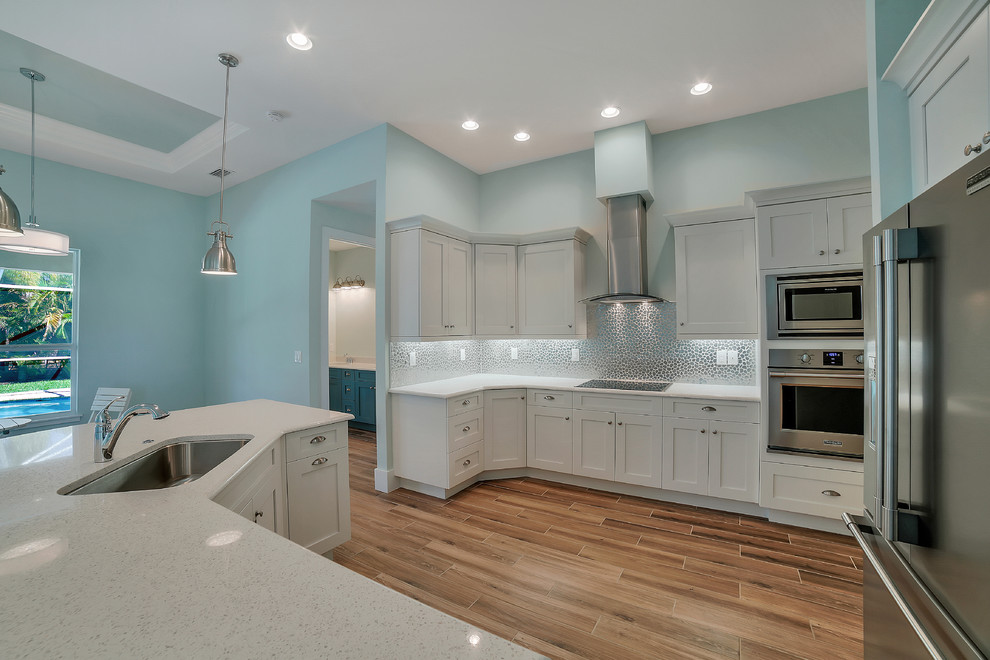 Mid-sized transitional u-shaped open concept kitchen photo with a drop-in sink, recessed-panel cabinets, white cabinets, quartzite countertops, multicolored backsplash, mosaic tile backsplash, stainless steel appliances and an island