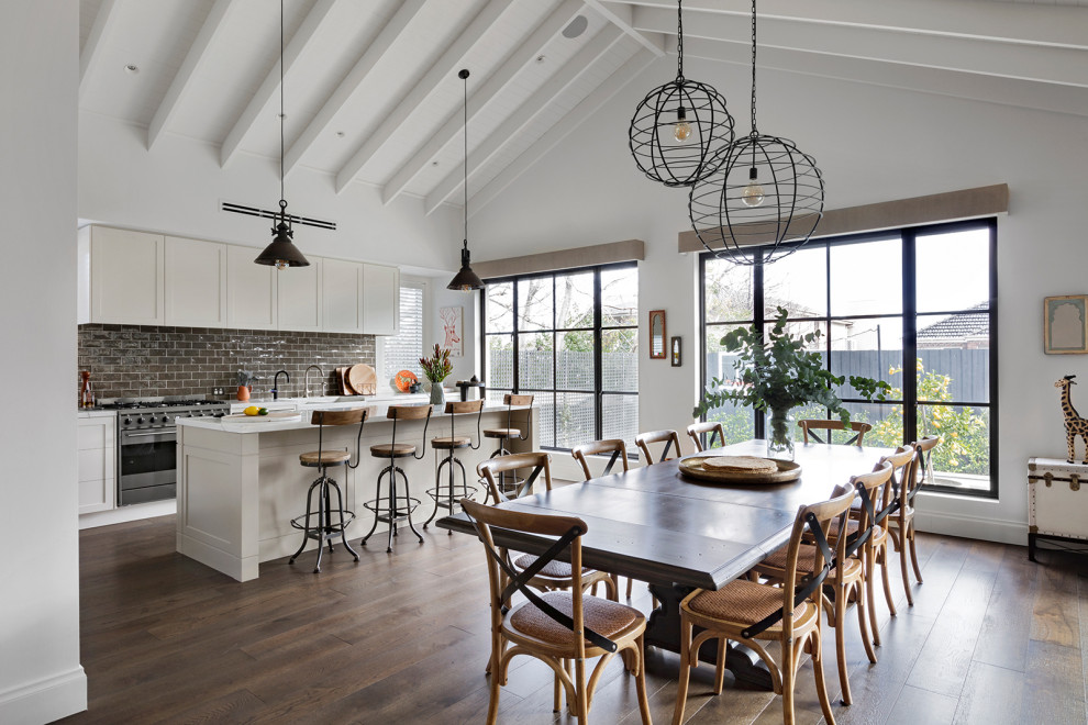Inspiration for a large country l-shaped eat-in kitchen in Melbourne with a farmhouse sink, raised-panel cabinets, white cabinets, marble benchtops, grey splashback, subway tile splashback, stainless steel appliances, medium hardwood floors, with island, brown floor, white benchtop and exposed beam.