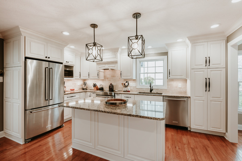Eat-in kitchen - mid-sized traditional l-shaped light wood floor and brown floor eat-in kitchen idea with an undermount sink, raised-panel cabinets, white cabinets, granite countertops, travertine backsplash, stainless steel appliances, an island, brown countertops and beige backsplash