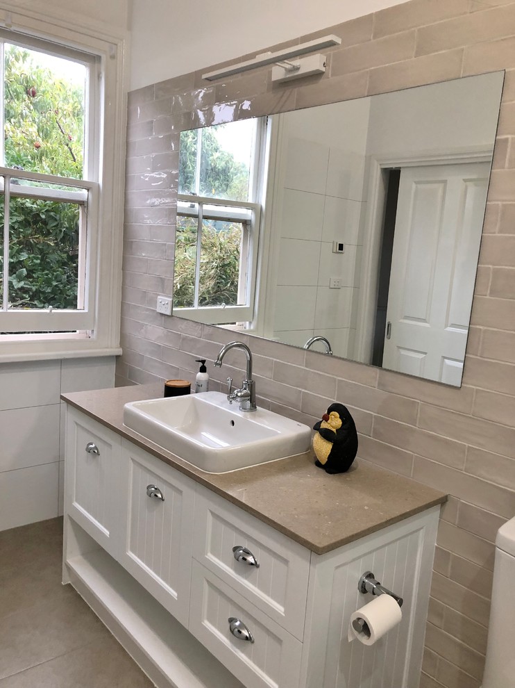 Photo of a mid-sized contemporary master bathroom in Other with furniture-like cabinets, white cabinets, an open shower, a two-piece toilet, beige tile, subway tile, beige walls, porcelain floors, a drop-in sink, solid surface benchtops, beige floor, an open shower and beige benchtops.